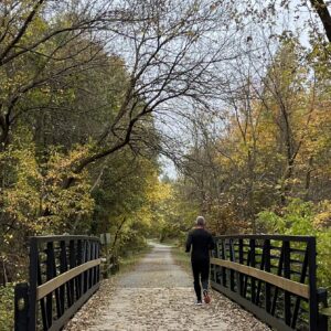 photo Out for a Jog - Taken on October 31, 2022, as my husband ran ahead on the foot bridge at the entrance of the park. I was lagging behind him on my bike and seeing him with the fall leaves behind him just solidified why we pack ourselves and drive to Kinder Park to get our exercise in...you can't complete with the beauty of the nature trail! by Kathy Hayes